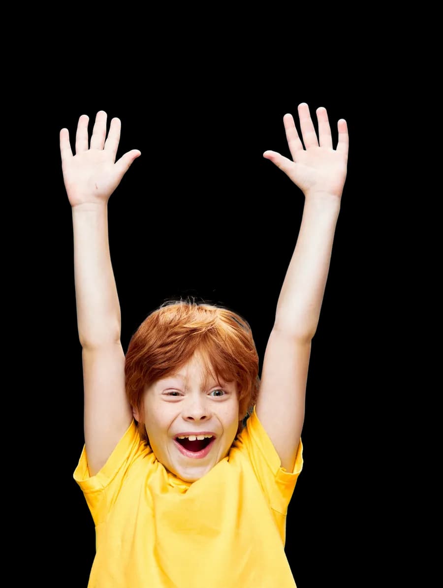 Excited child in a yellow T-shirt smiling with both arms raised